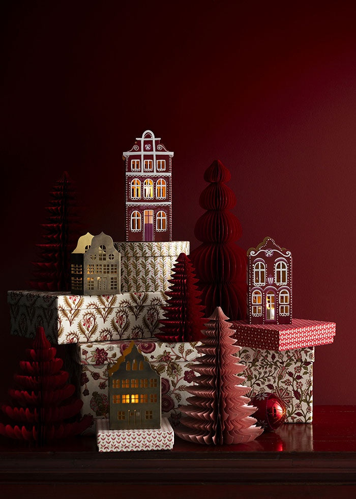 Paper trees placed on patterned gift boxes alongside illuminated miniature houses
