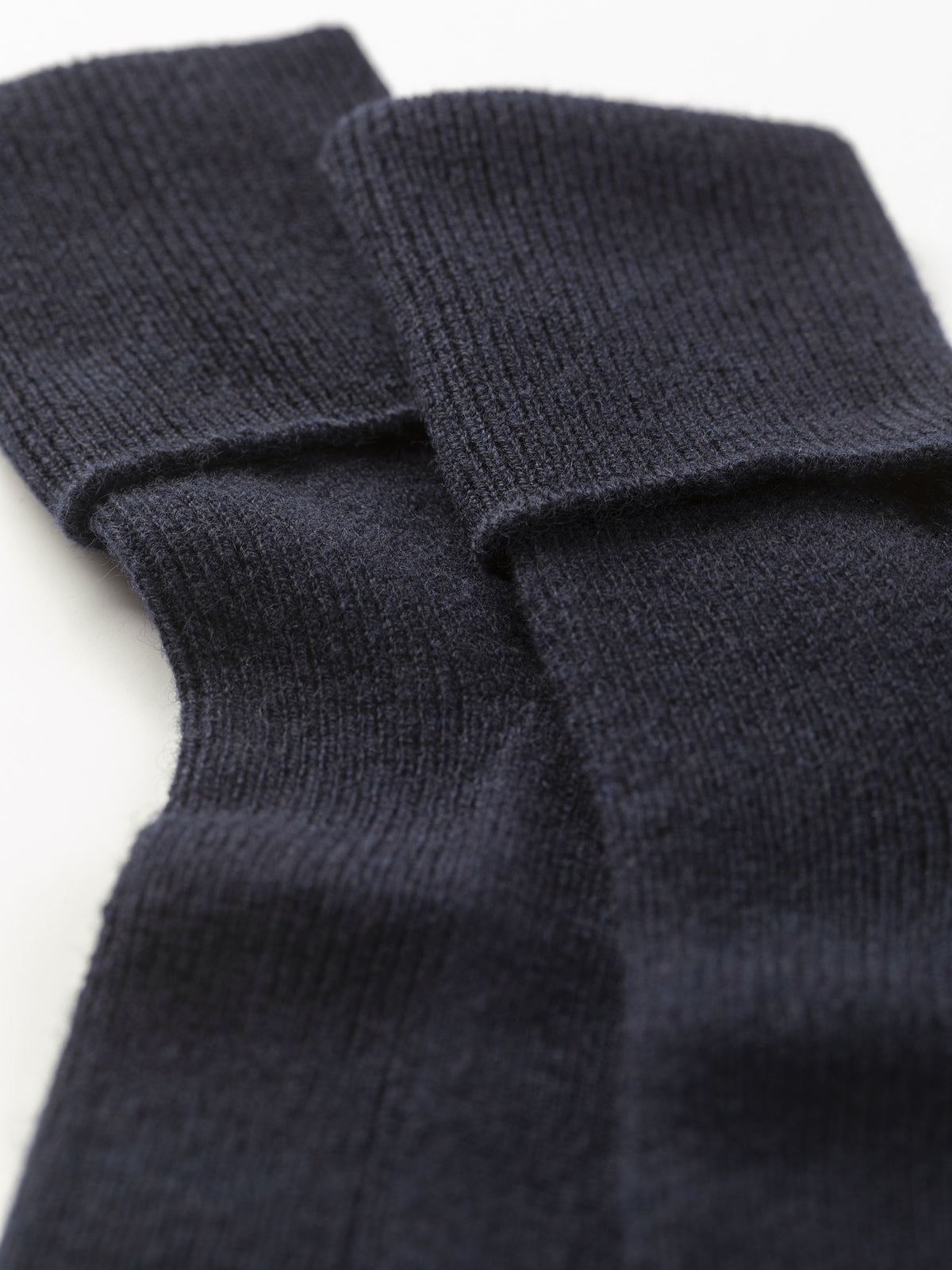 Close-up of the folded cuffs showing the fine ribbed knit texture of the dark navy cashmere socks