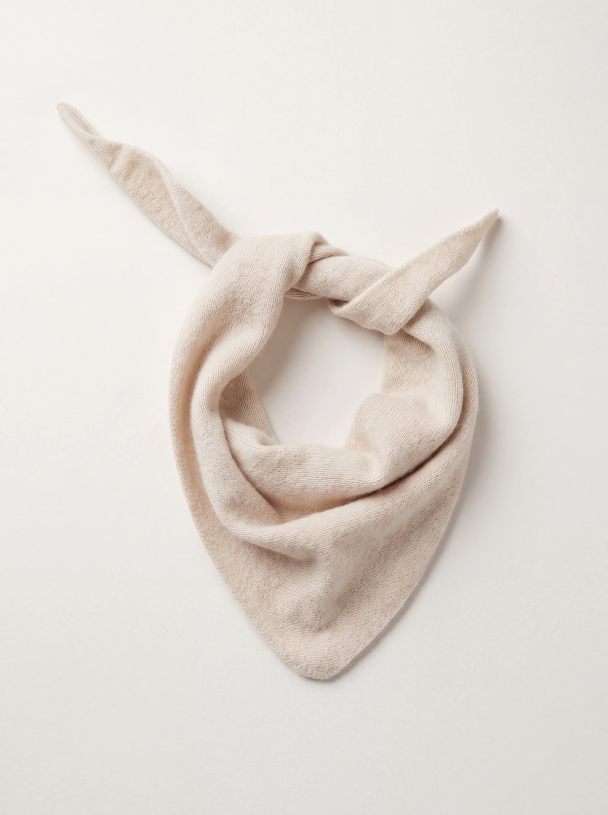 Knitted ivory wool bandana folded into a triangle with tapered ends tied loosely at the top