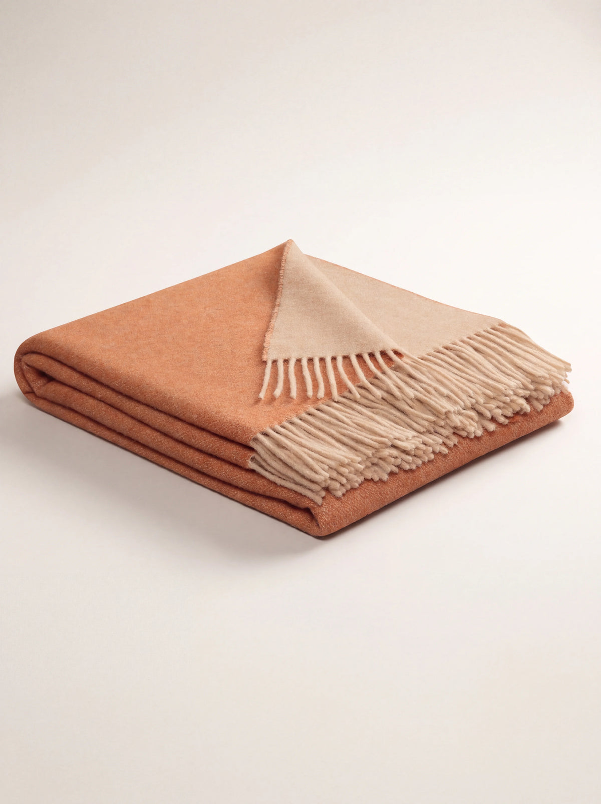 Reversible wool and cashmere blanket folded, showing terracotta side, sand reverse and fringe