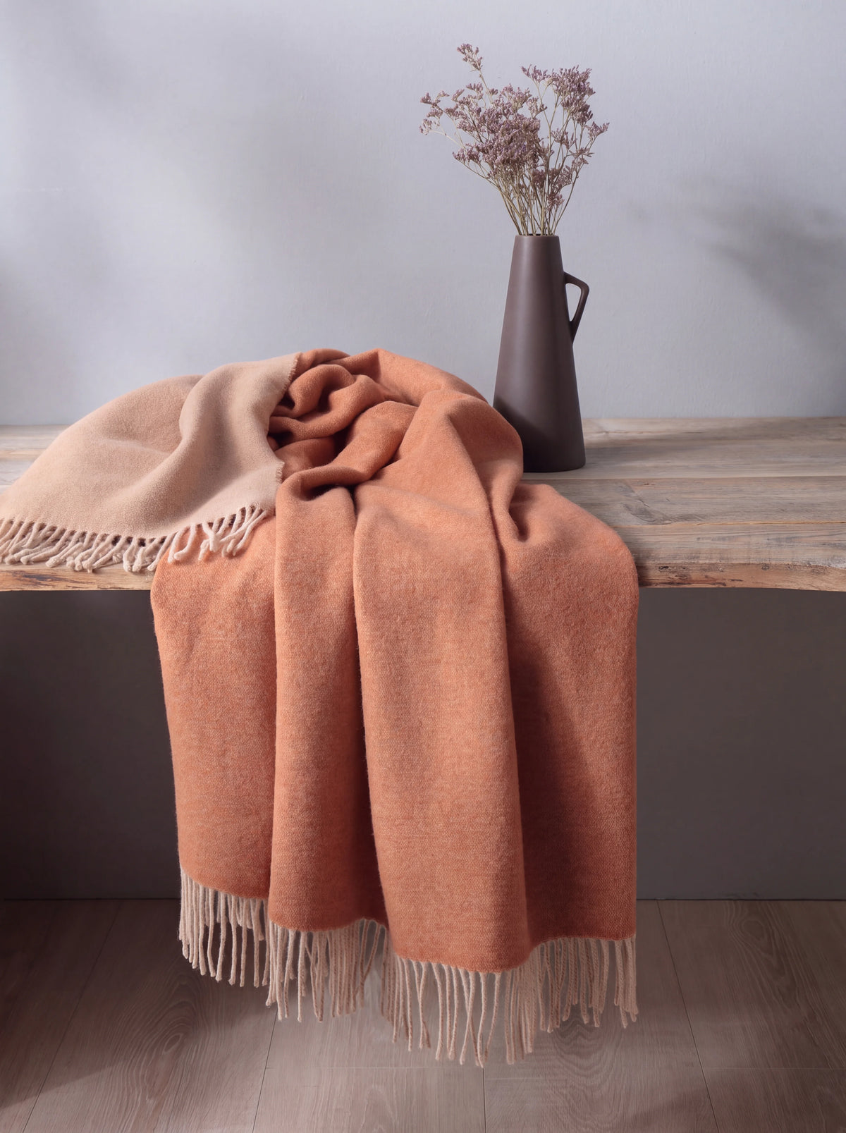 Reversible wool blanket draped loosely over a wooden bench, showing its drape and fringed hem