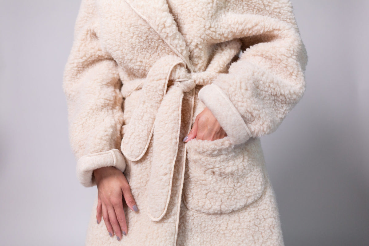 Close-up of the beige wool dressing gown showing the knotted tie belt, folded cuff and patch pocket