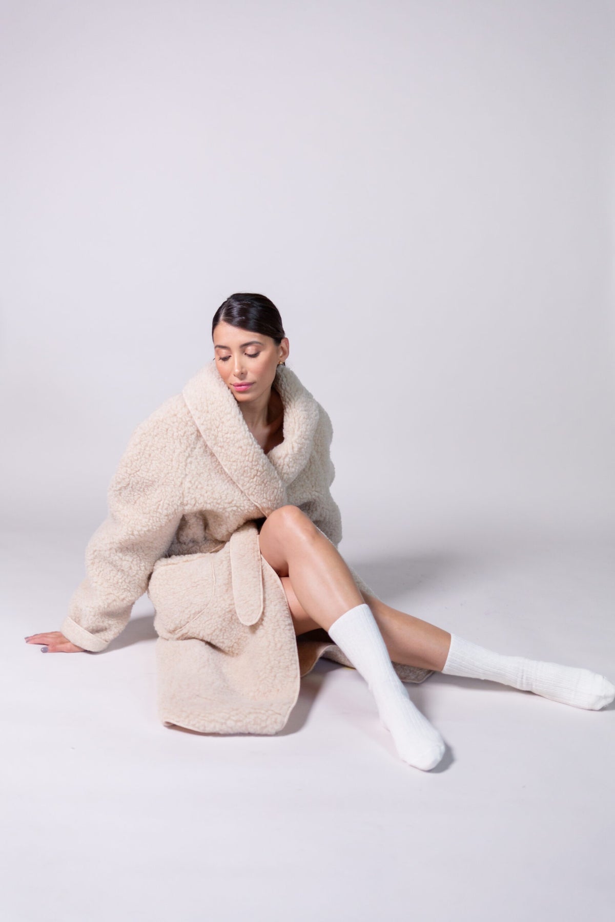 Beige wool dressing gown worn seated, showing its knee length and relaxed wrap fit