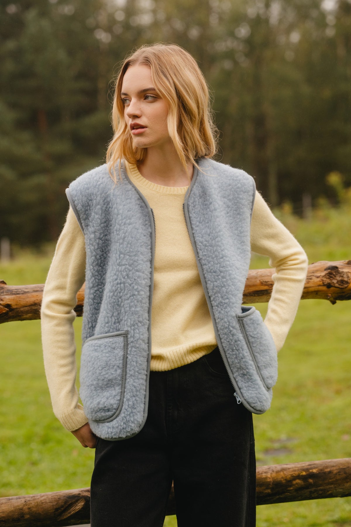Icy blue merino wool fleece vest worn open, showing the front zip, patch pockets and piped edges