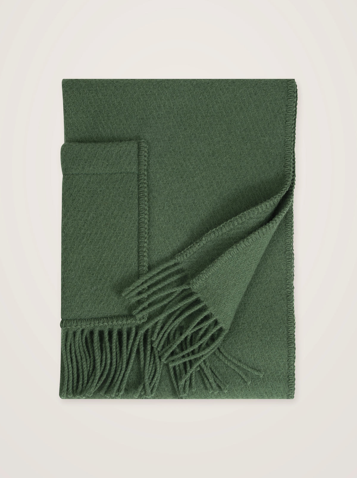 Dark moss green wool pocket shawl neatly folded, displaying the woven texture, tasseled trim and patch pocket