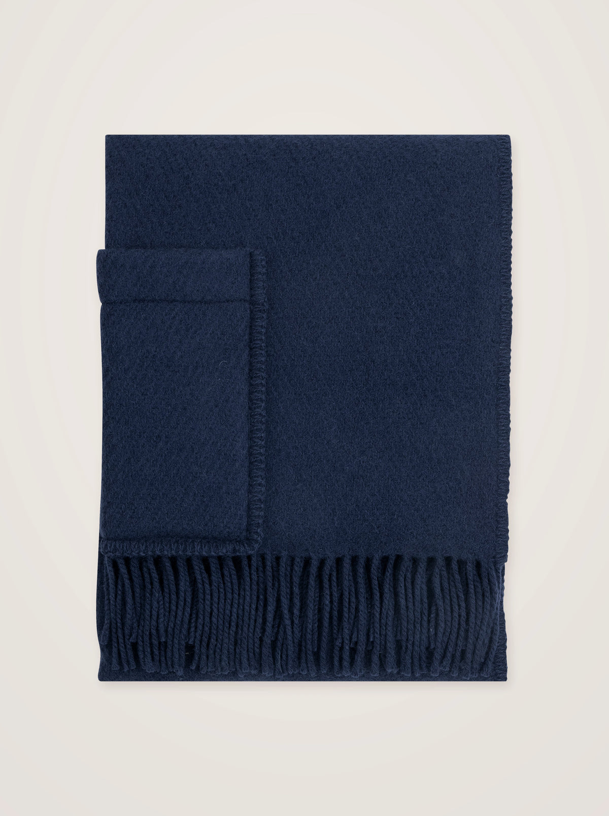 Midnight blue wool pocket shawl folded flat, showing the stitched patch pocket and fringed hem