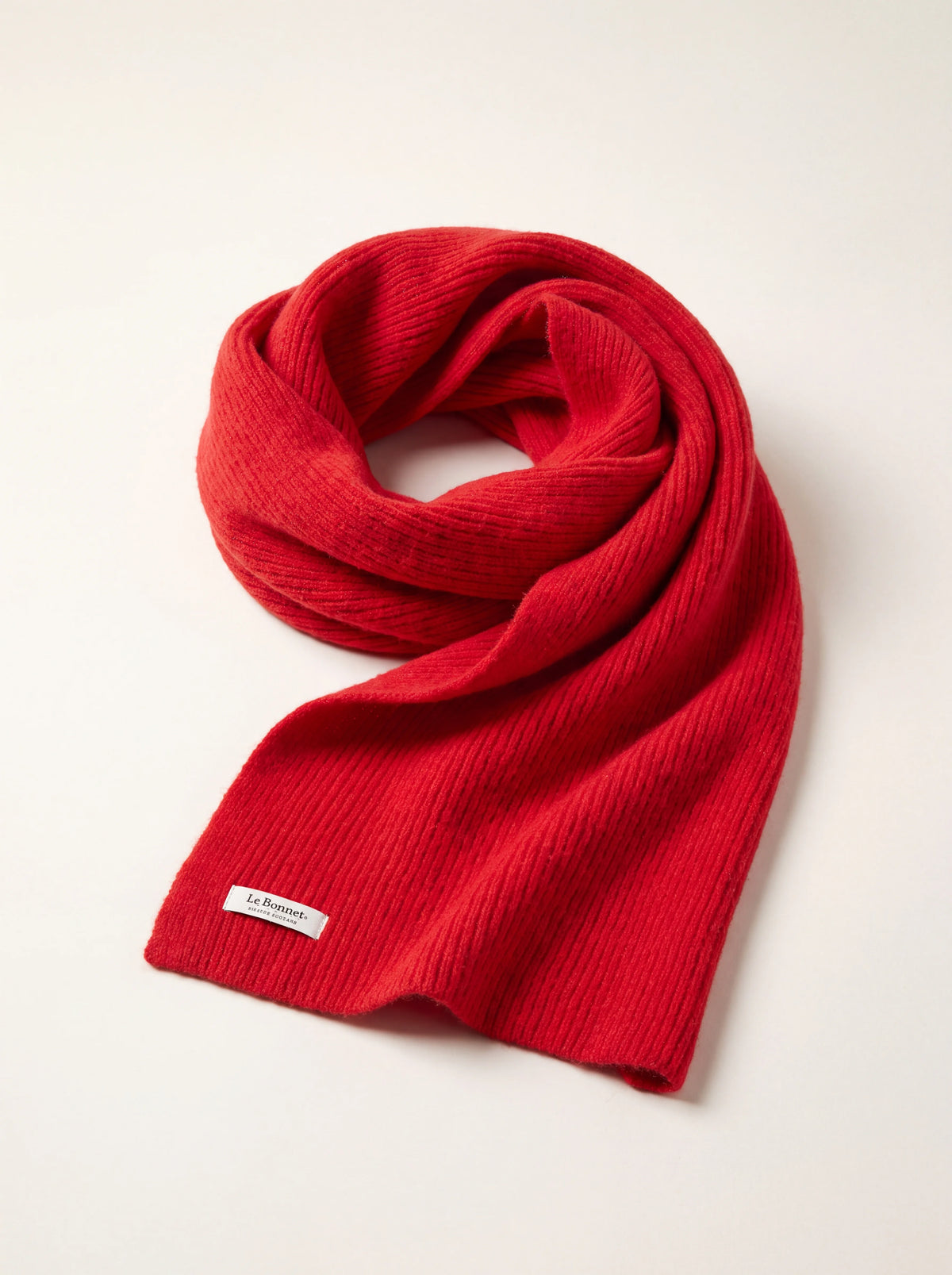 Crimson ribbed knit wool scarf looped loosely, showing the stitched Le Bonnet label at the hem