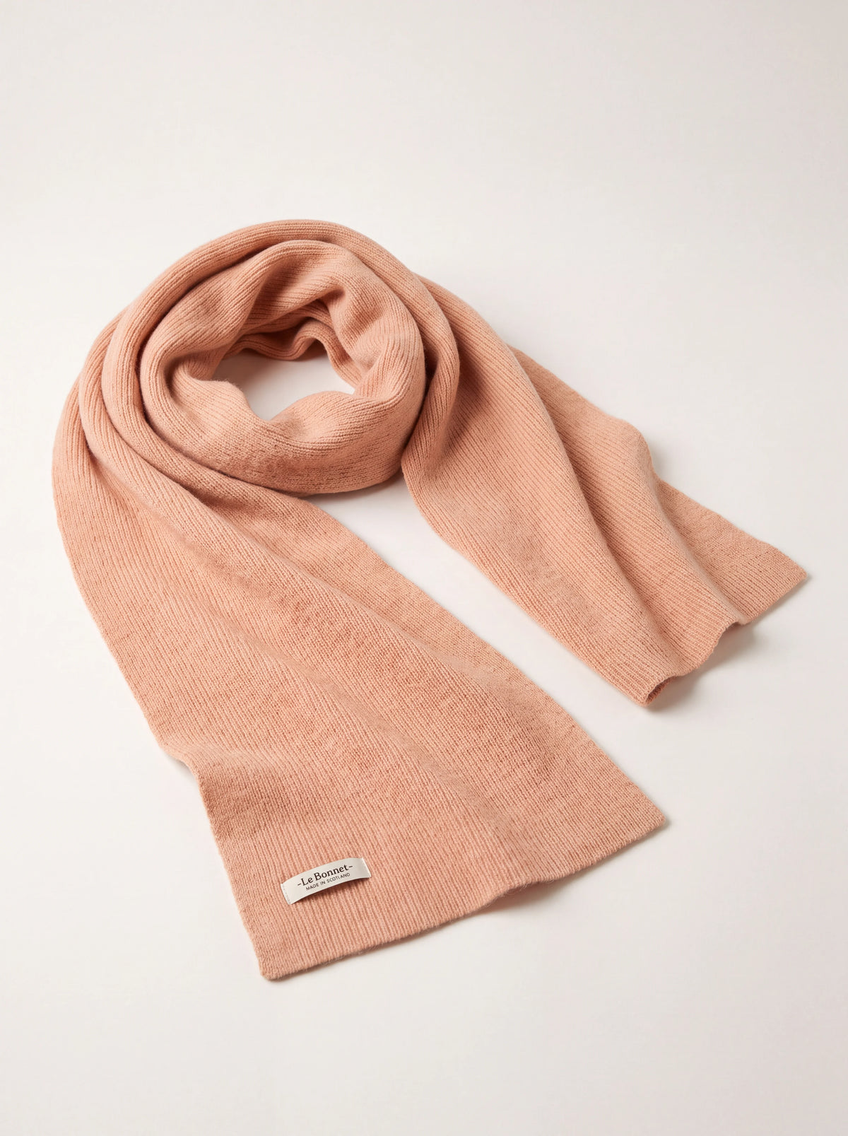 Peach ribbed wool scarf loosely looped, showing a woven label reading -Le Bonnet- MADE IN SCOTLAND