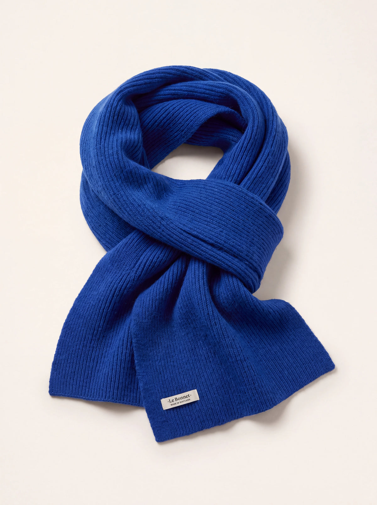 Ribbed azure blue wool scarf folded in a loop, with a label reading -Le Bonnet- MADE IN SCOTLAND