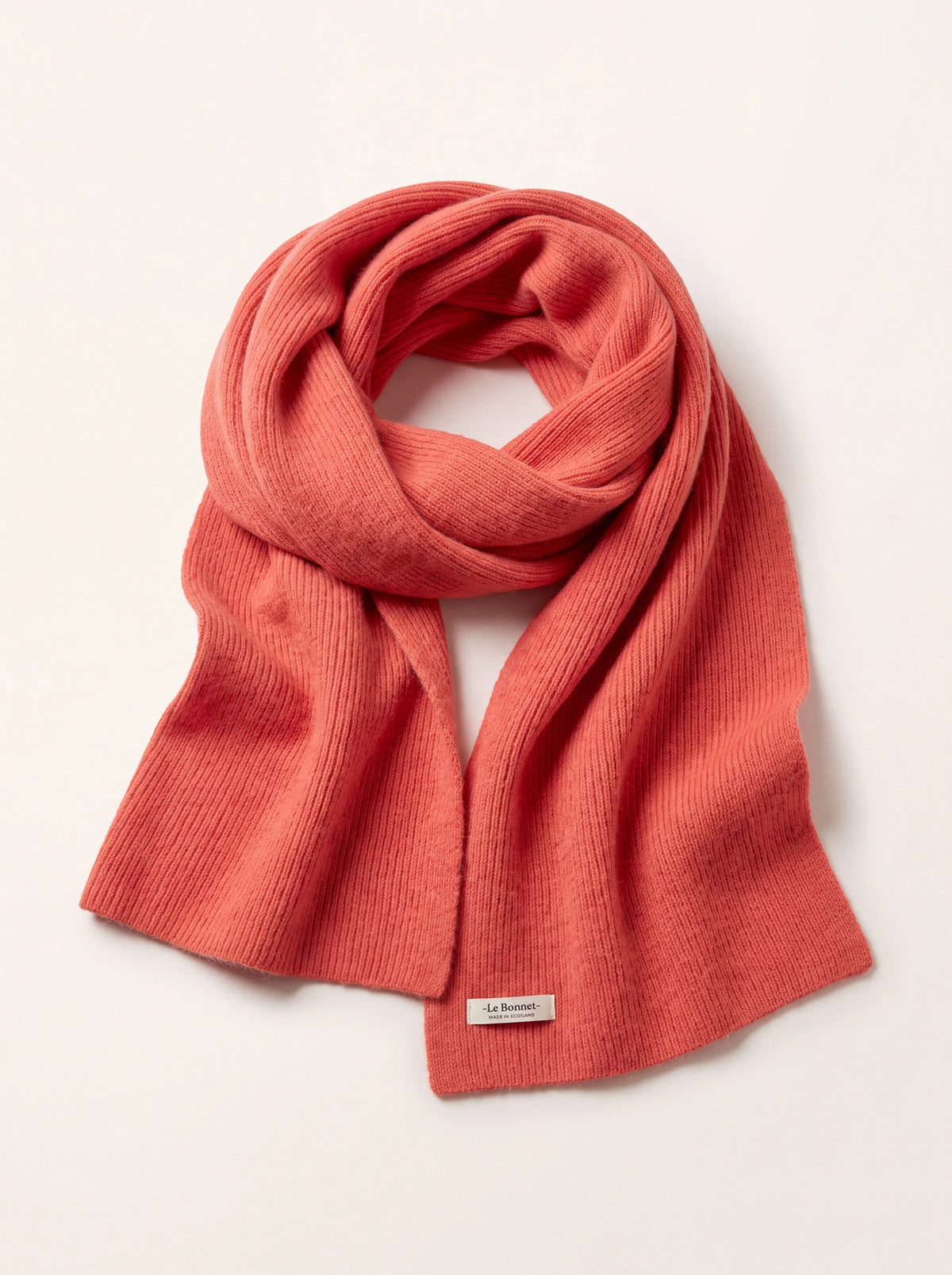 Salmon-pink ribbed lambswool scarf looped once, with a label reading '-Le Bonnet- MADE IN SCOTLAND