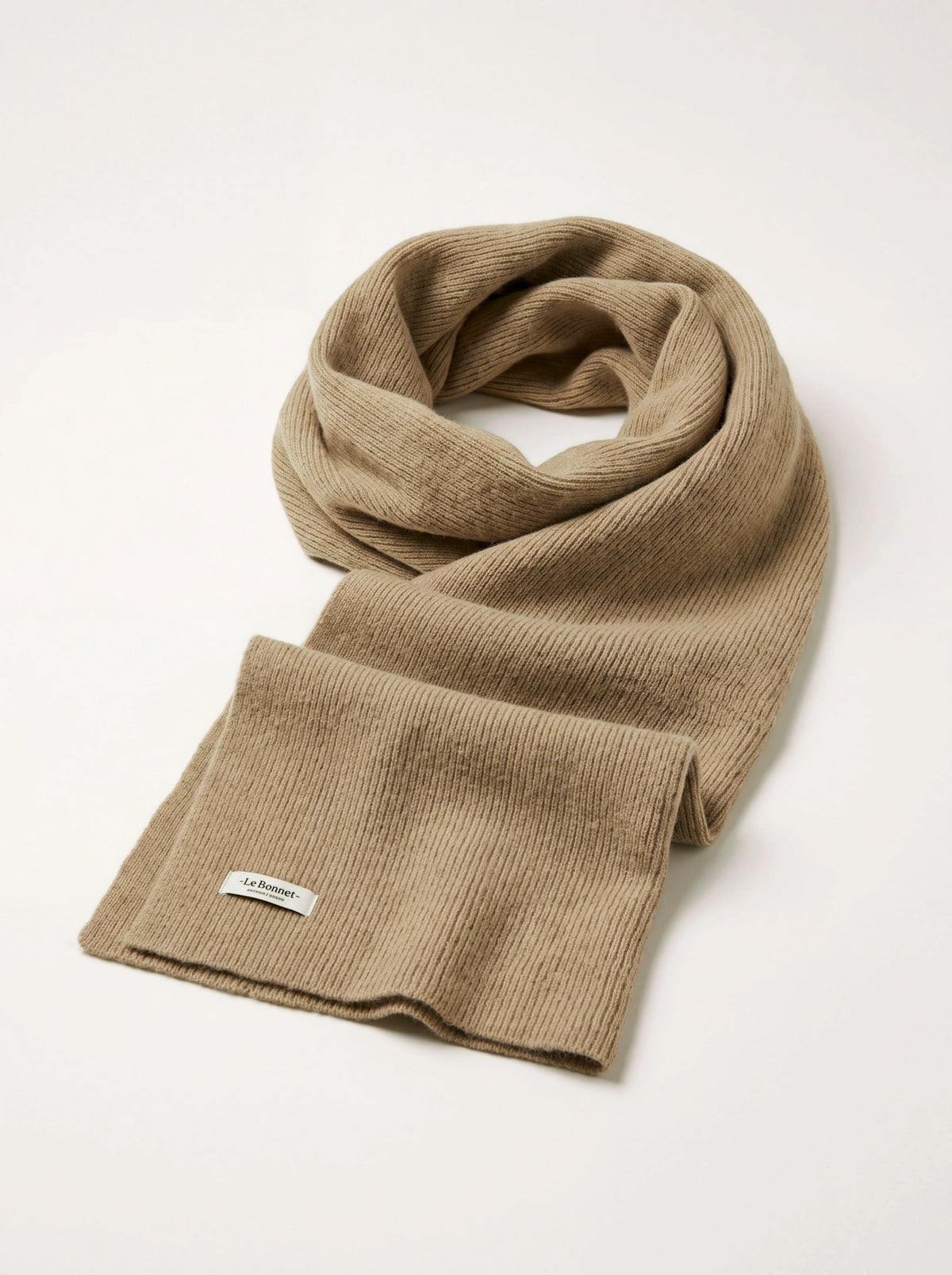 Ribbed sand wool scarf looped loosely, showing the woven -Le Bonnet- label stitched near the hem