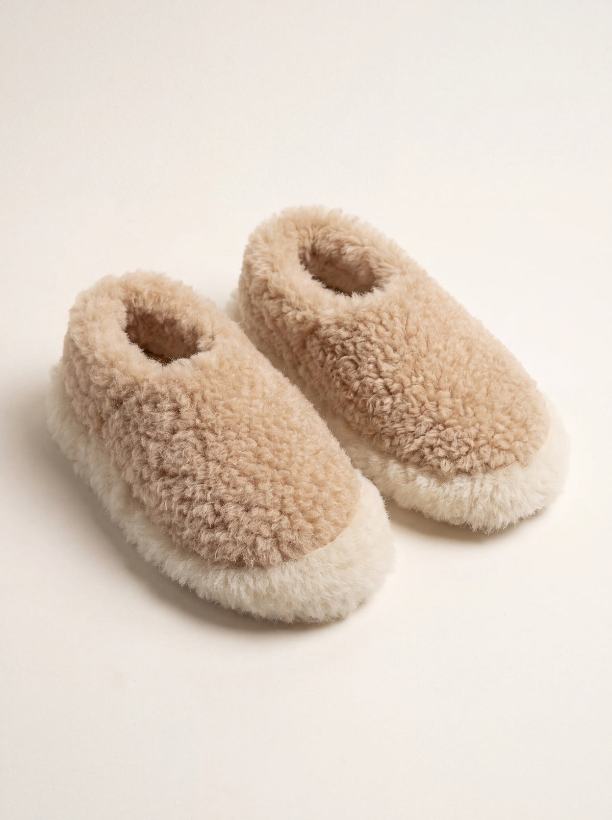 Beige sheep wool slippers with rounded toes and a thick off-white wool trim along the soles