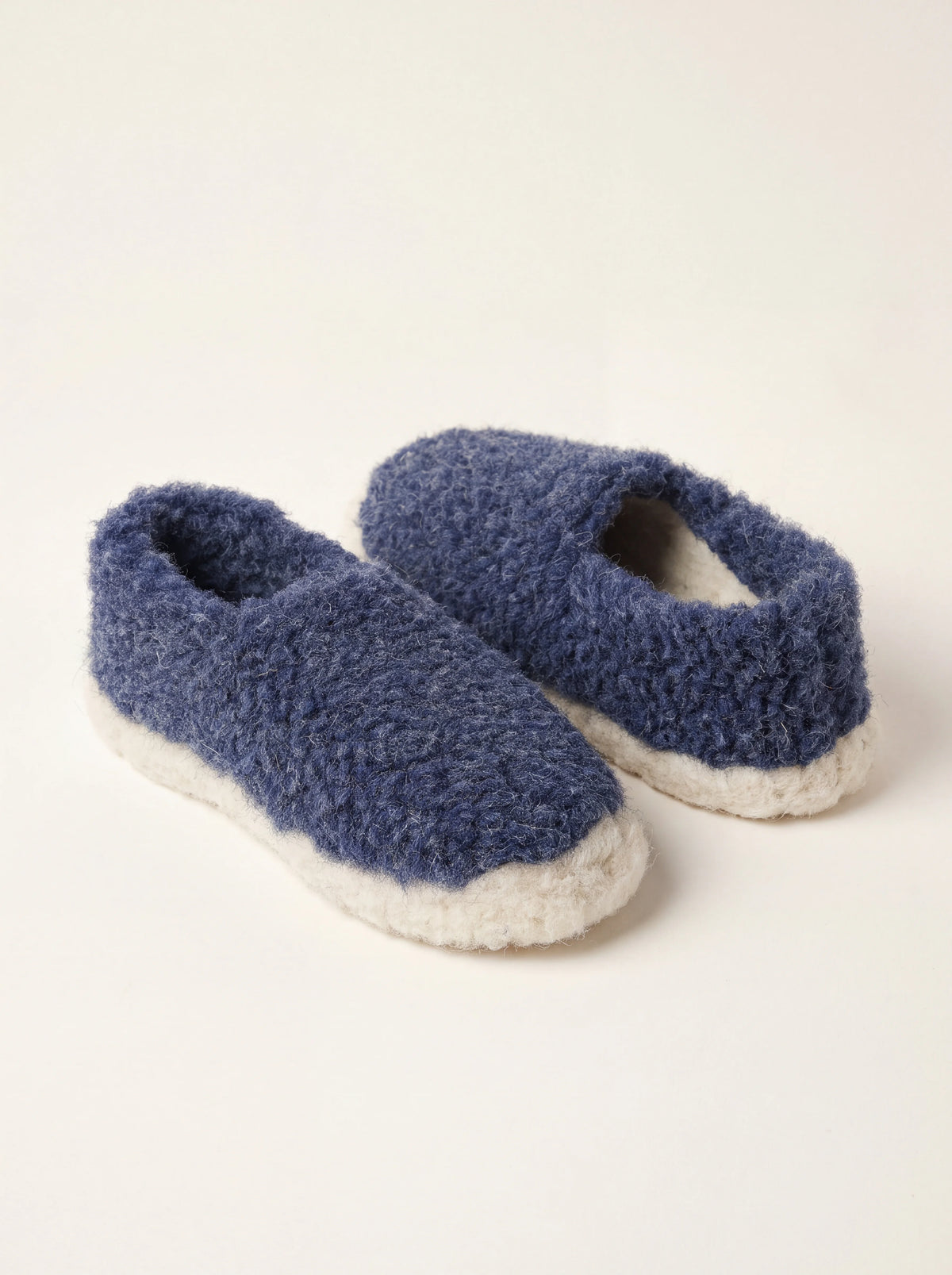 Dark blue sheep wool slippers with a curly fleece finish and contrasting off-white soles