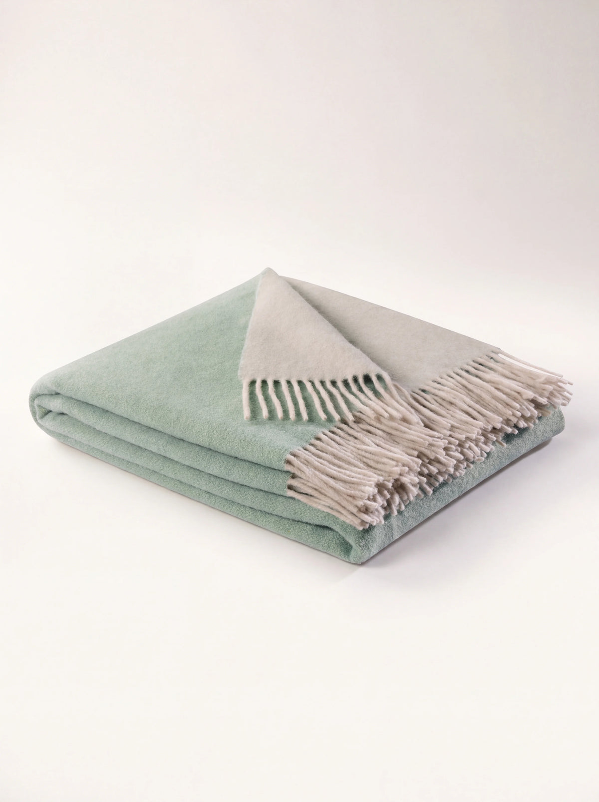 Wool and cashmere throw in sage green, folded to show the cream reverse and fringed edges