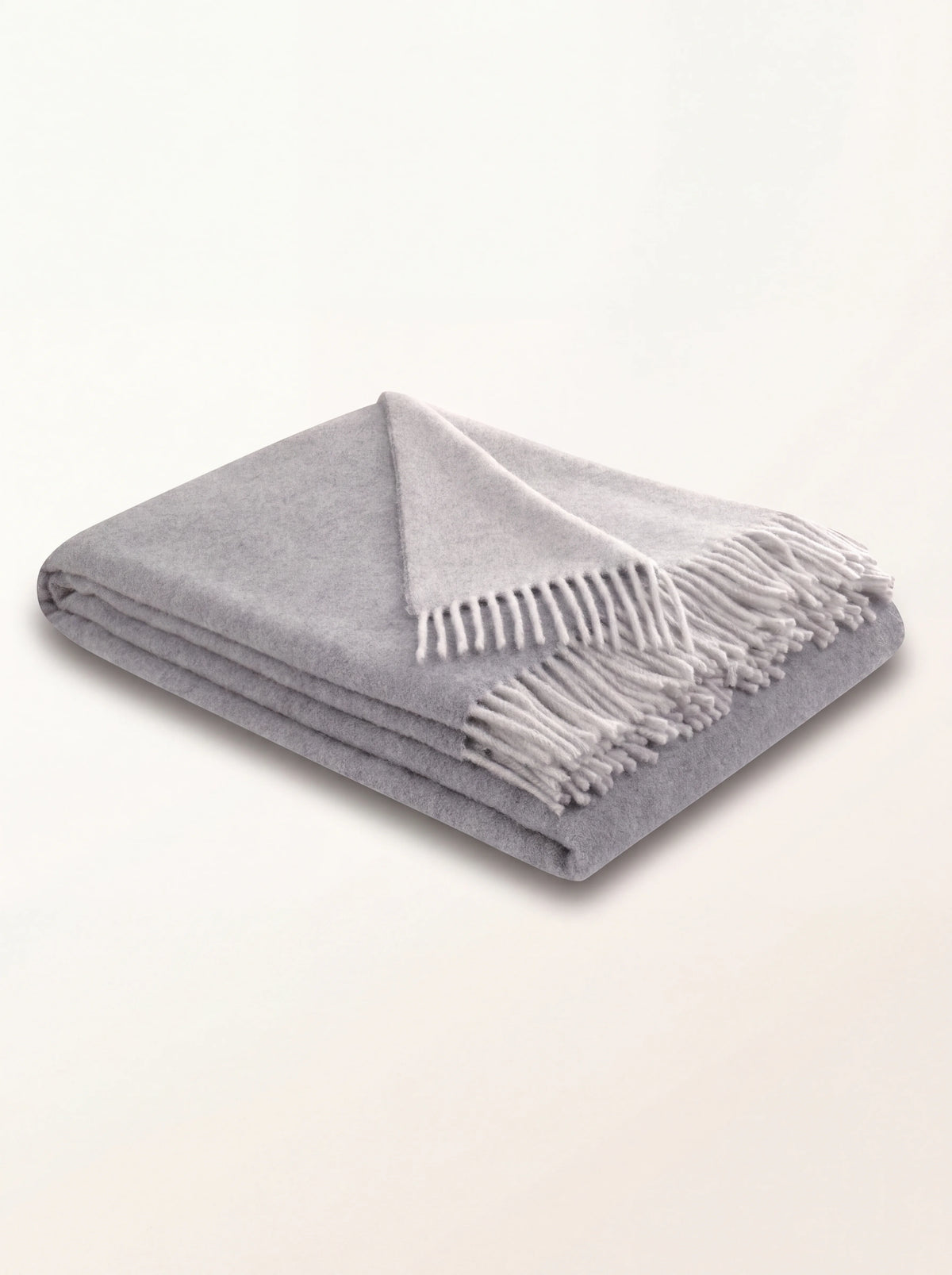 Folded light grey wool and cashmere throw with fringe and a turned corner showing the lighter reverse