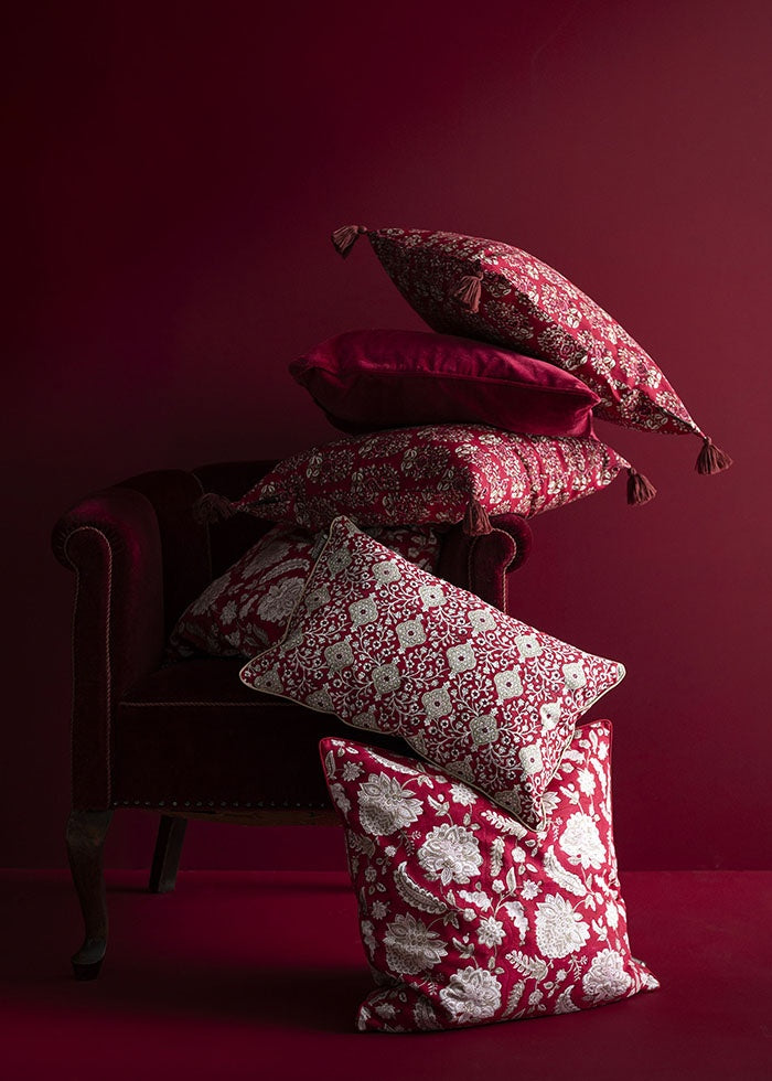 Raspberry floral cushion placed on the floor beside an armchair stacked with patterned cushions