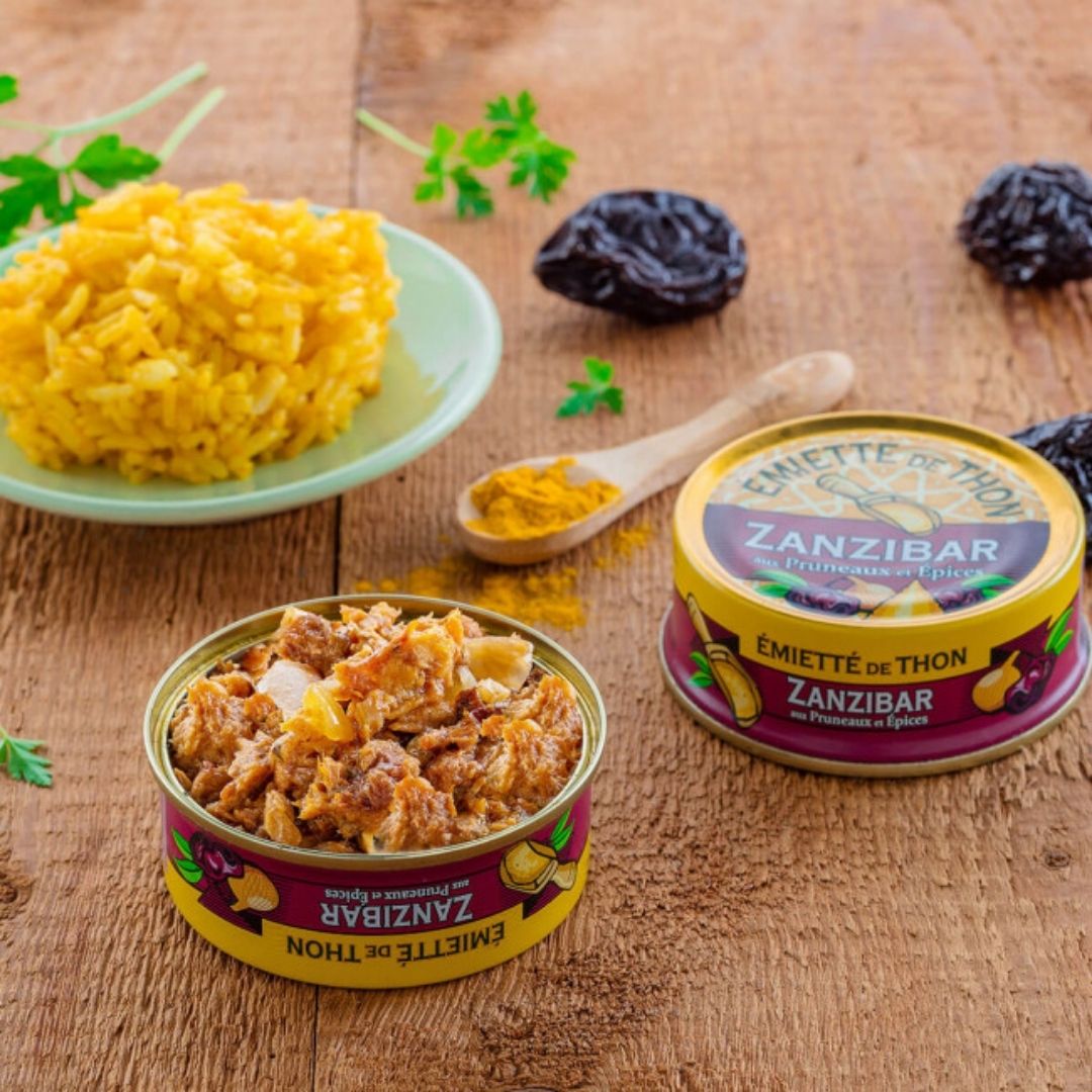 Open tin showing textured flaked tuna beside an unopened tin, spiced rice, whole prunes and spice powder