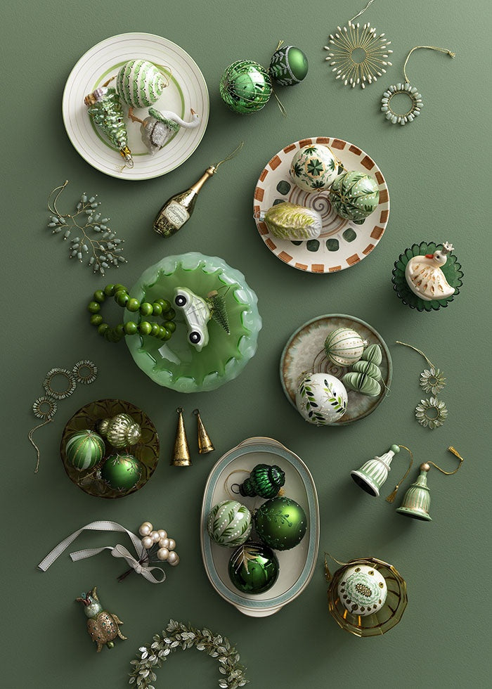 Beaded twig ornament shown among an assortment of green and white Christmas decorations and tableware